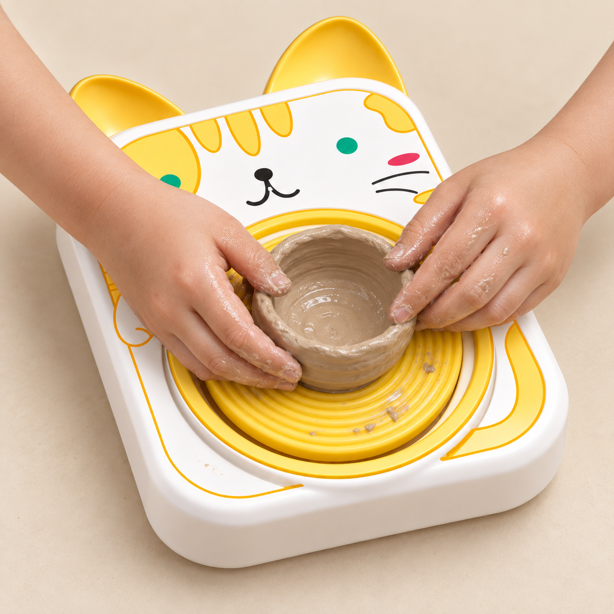 Child's hands shaping a small clay bowl on the cat-design mini pottery wheel