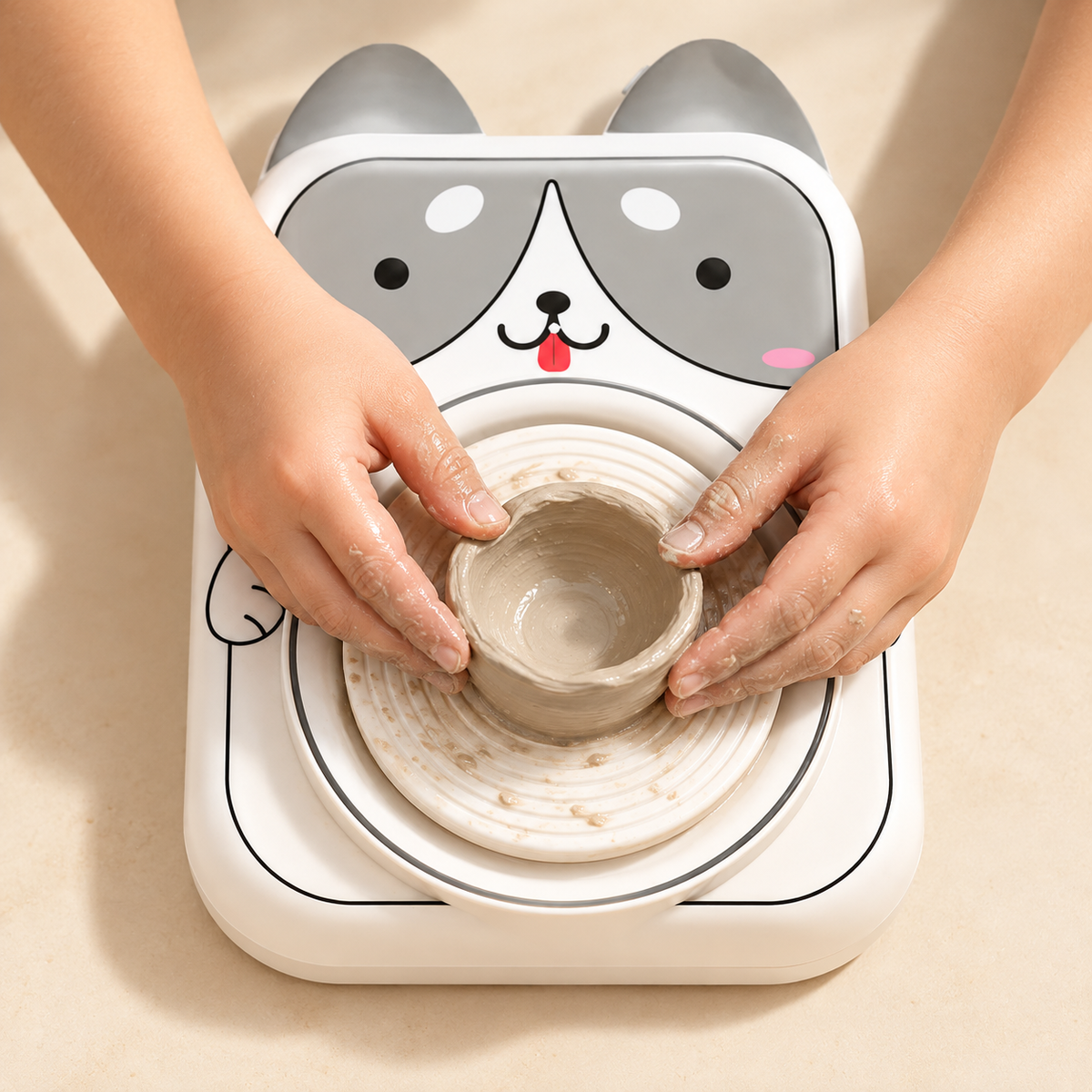Child's hands shaping a small clay bowl on the dog-design mini pottery wheel